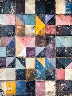 Weathered geometric patchwork pattern with colorful squares and triangles in pink, blue, yellow, and dark tones