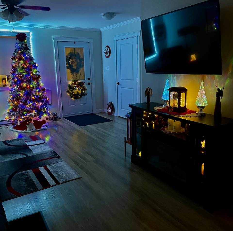 Living room with a lit Christmas tree, wreath on the door, and glowing holiday decorations