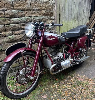 Vintage maroon Douglas motorcycle parked beside a stone wall and wooden door