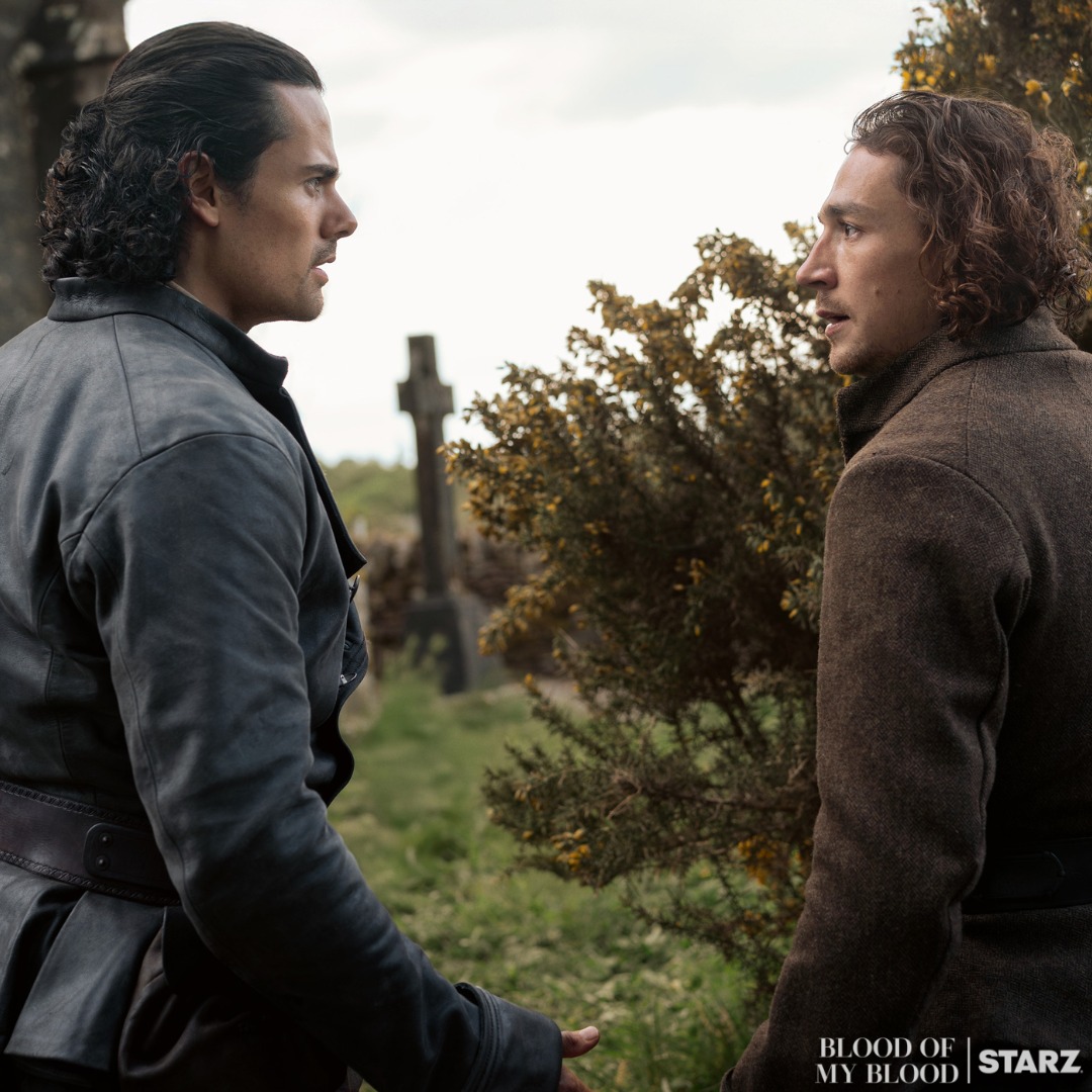Two men in historical clothing having a serious conversation outdoors with trees in background
