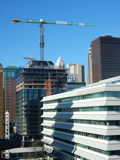 Green construction crane towering over modern office buildings and city skyline against blue sky