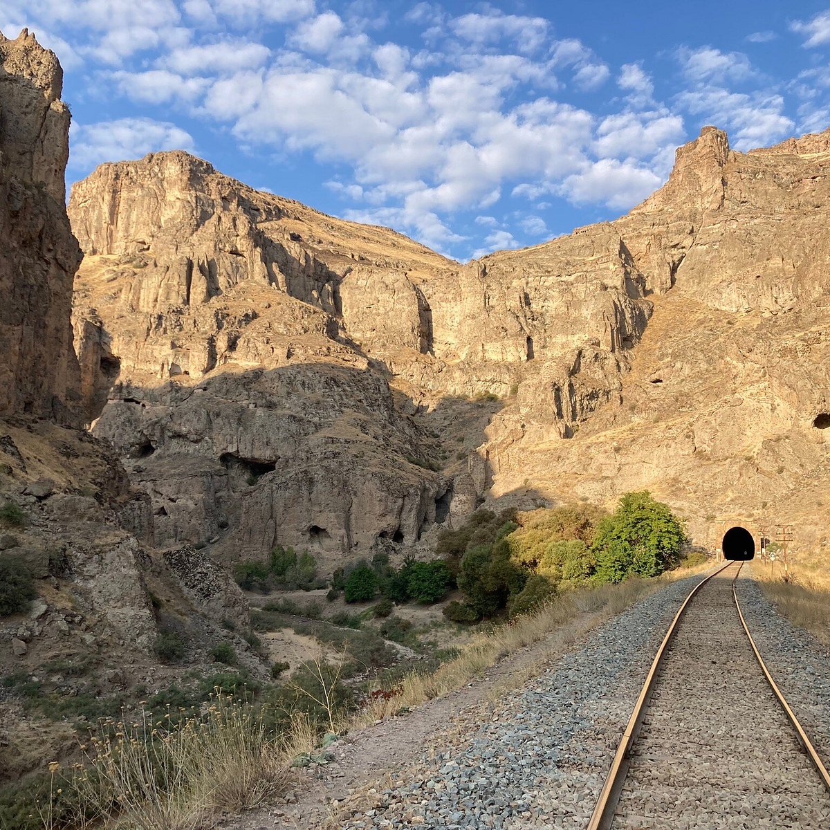 Railway tracks leading to a tunnel through a rocky canyon beneath a blue sky