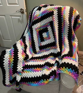 Multicolored granny square crochet blanket with rainbow stripes draped on white chair