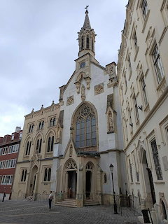 Gothic church with tall spire on a cobblestone square surrounded by historic European buildings