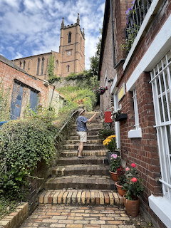Stone steps ascending between brick buildings toward a church tower, with flower pots lining the stairway