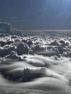 Aerial view of dense white clouds seen from above with sunlight piercing through dark sky