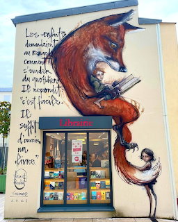 Street art mural of large red fox wrapped around girl reading book on bookstore wall