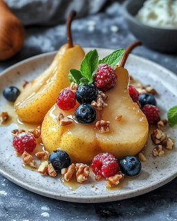Poached pear halves topped with fresh berries, mint leaves, and walnuts on a white plate