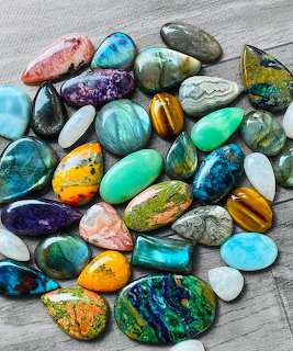 Collection of polished gemstones in blue, green, orange, purple and pink tones on wooden background
