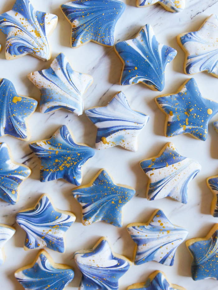 Star-shaped cookies decorated with blue and gold marbled icing on white background