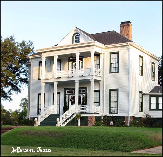 Historic white two-story house with columns, porches, and a grassy lawn in Jefferson, Texas