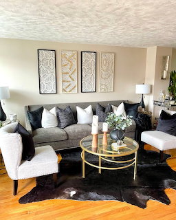 Modern living room with gray sofa, white chairs, gold coffee table, cowhide rug, and decorative wall panels