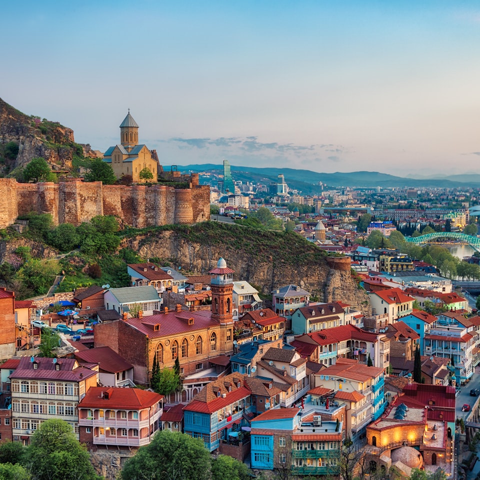 Aerial view of Tbilisi old town with colorful houses, fortress walls and church at sunset