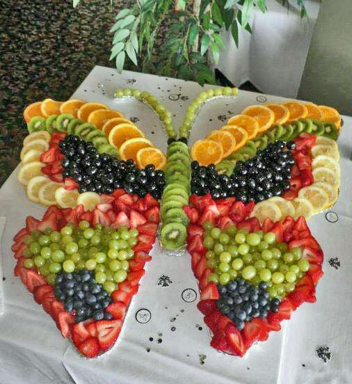 Colorful fruit platter arranged in a butterfly shape with strawberries, grapes, oranges, kiwi, and blueberries