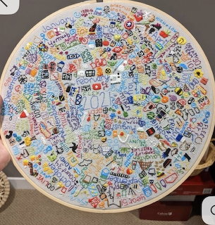Circular embroidery hoop with dense colorful stitched text, doodles, and floral patterns on fabric