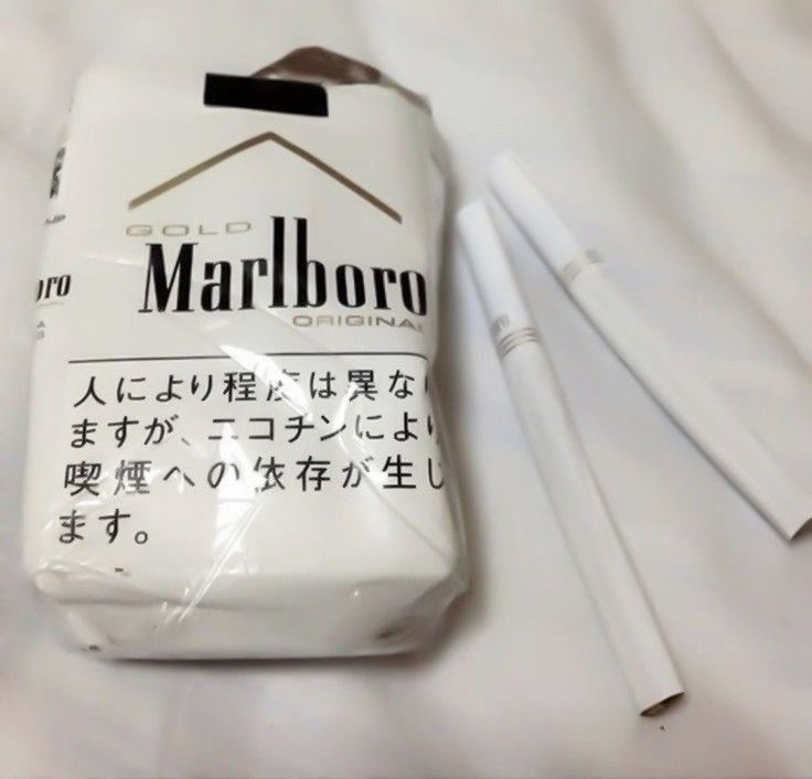 White cigarette pack with Japanese text next to two cigarettes on white fabric