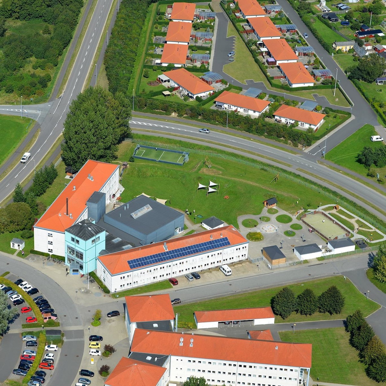Aerial view of a school campus with orange roofs, roads, parking lot, and grassy grounds
