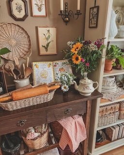 Cozy vintage cottage interior with flowers, botanical prints, baskets, and rustic wooden table decor