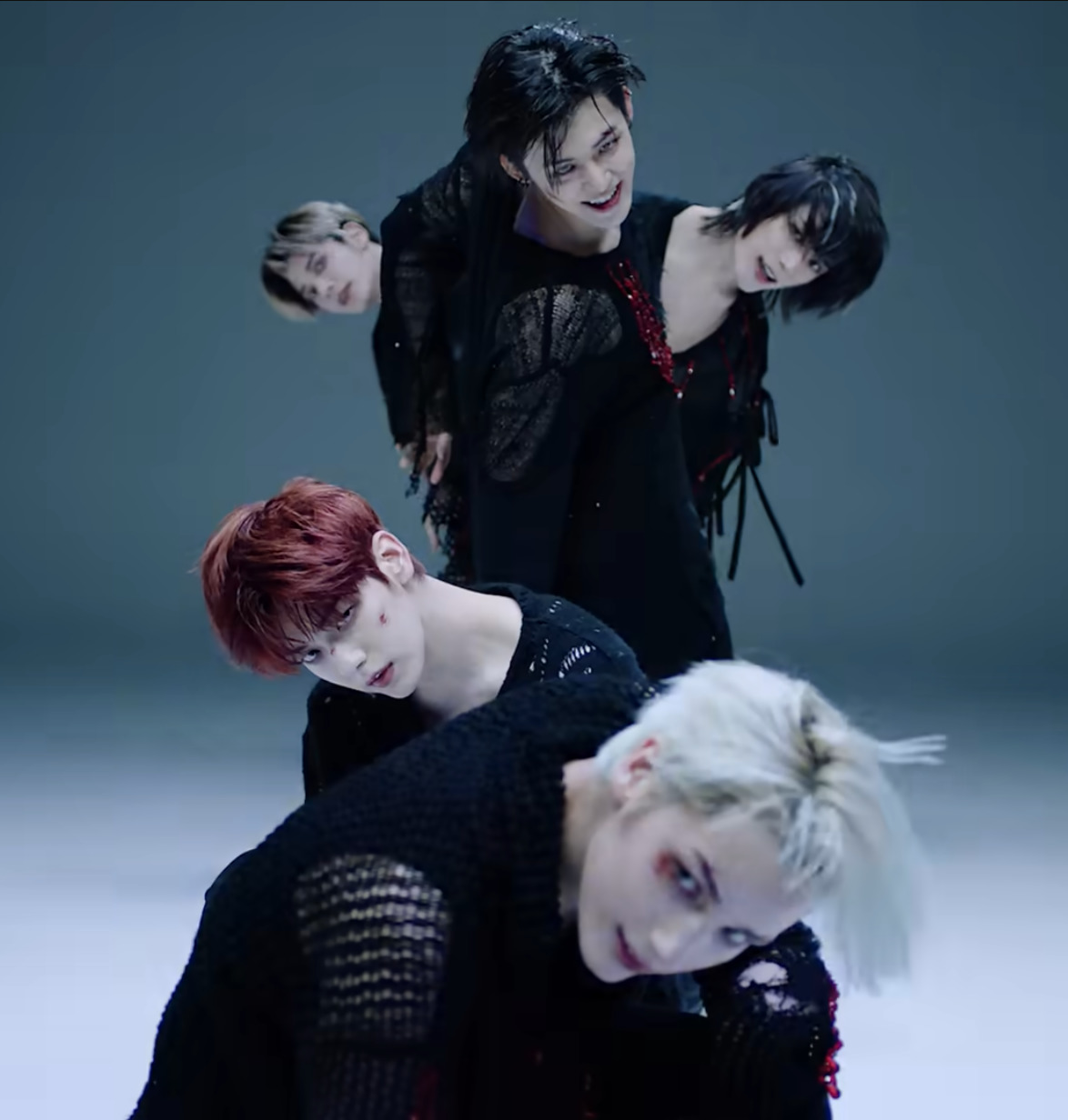 Four TXT members in black clothing posed artistically in studio with moody lighting