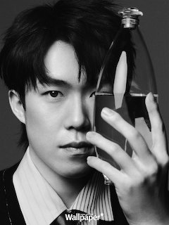 Black and white close-up portrait of a young Asian man holding a glass perfume bottle near his face