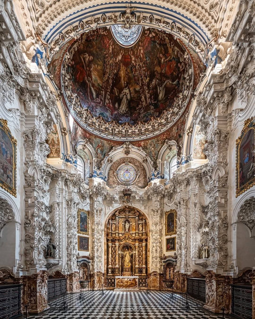 Ornate baroque church interior with frescoed ceiling, white stucco columns, and gilded altar