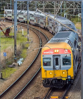 Orange and white passenger train on curved tracks at station with overhead wires