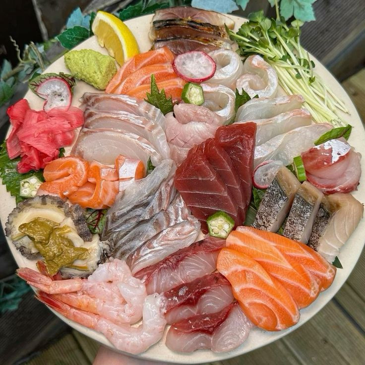 Round platter of assorted raw fish sashimi with salmon, tuna, shrimp, garnished with lemon and vegetables on ice