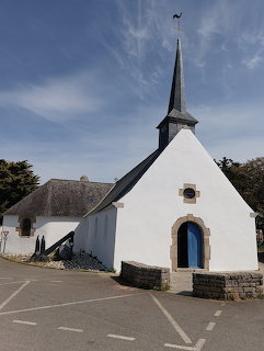 Small white chapel with dark steeple and arched blue door in a French village on a sunny day