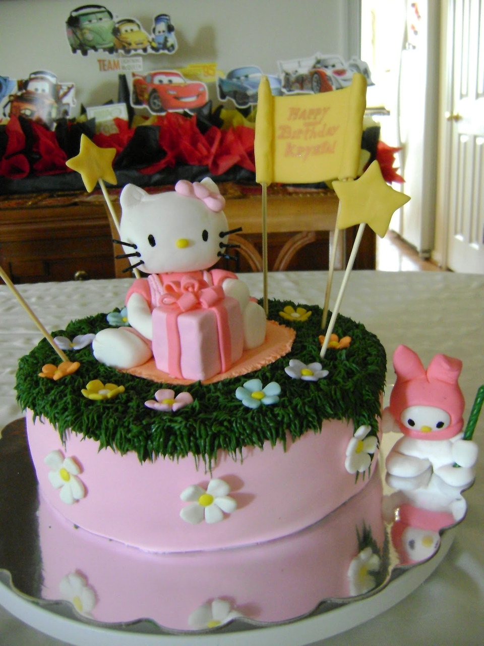 Pink two-tier birthday cake with Hello Kitty character figure centerpiece and floral decorations
