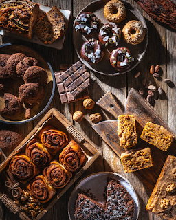 Overhead view of assorted bakery items like cinnamon rolls, donuts, cookies and cake on a rustic wooden table