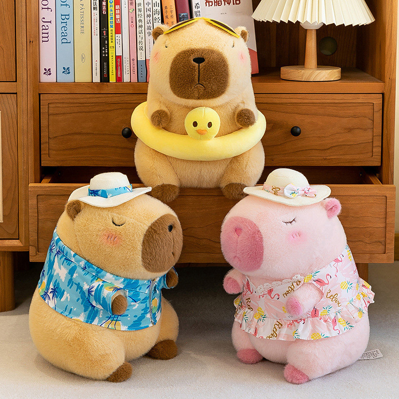 Three cute capybara stuffed animals wearing colorful summer clothing and swim accessories