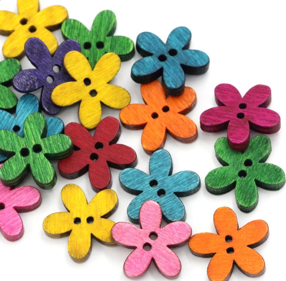 Collection of colorful wooden flower-shaped buttons with two holes, arranged in a scattered pattern on white surface