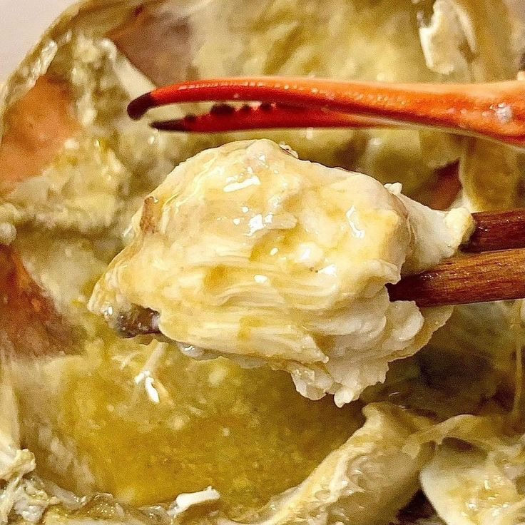 Chopsticks lifting white crab meat from inside a cracked crab shell