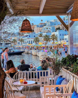 Waterfront restaurant terrace overlooking Naxos harbor with white buildings and palm trees at dusk