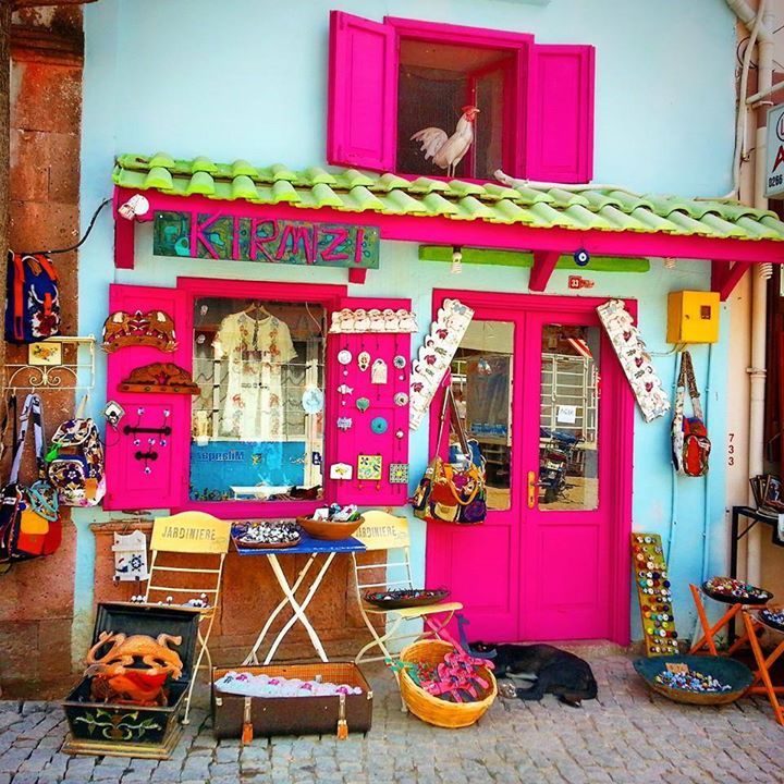 Bright pink and green thrift shop exterior with colorful merchandise displayed outside and a white rooster in the window