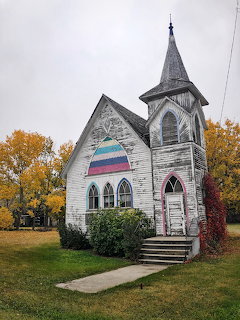 White church with pointed steeple and Gothic arched windows surrounded by fall trees