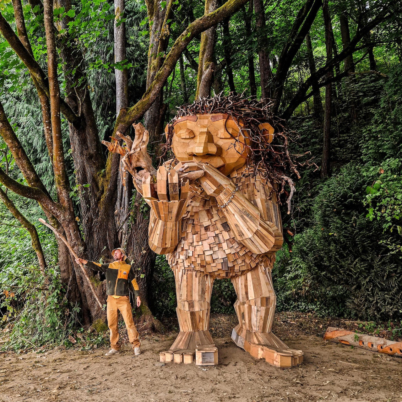 Large wooden troll sculpture in a forest with a person standing beside it