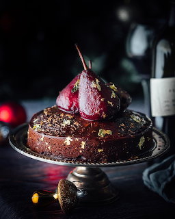 Chocolate cake with poached red pear on top, decorated with gold leaf on a glass cake stand