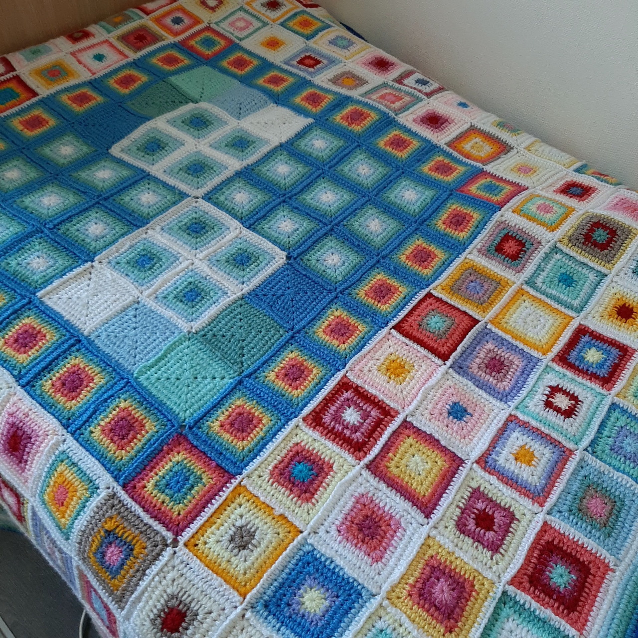 Colorful crocheted patchwork blanket with multicolored square patterns on a bed