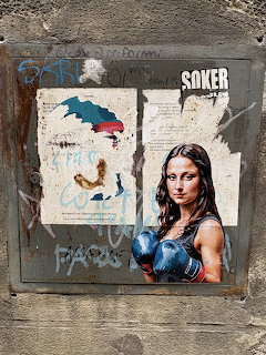 Street art of woman with boxing gloves beside graffiti-covered Mona Lisa poster on old textured wall