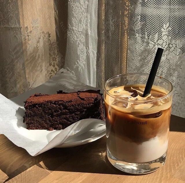 Layered iced coffee in a glass beside a chocolate brownie on a table
