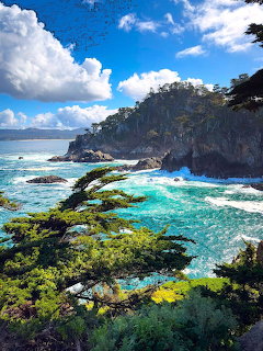 Rocky coastal cliffs with turquoise water and green algae-covered rocks under blue sky with white clouds