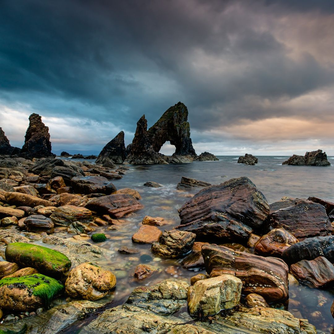 Rocky coastal landscape with natural stone arch and sea stacks under dramatic cloudy sky