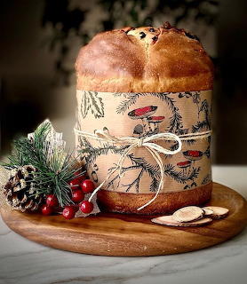Panettone Christmas bread in illustrated wrapper with pine branches, red berries, and pinecone on wooden serving board
