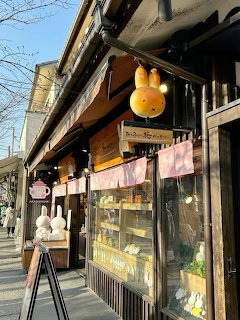 Cafe storefront on a city street with a hanging bunny sign, pink awnings, and display windows
