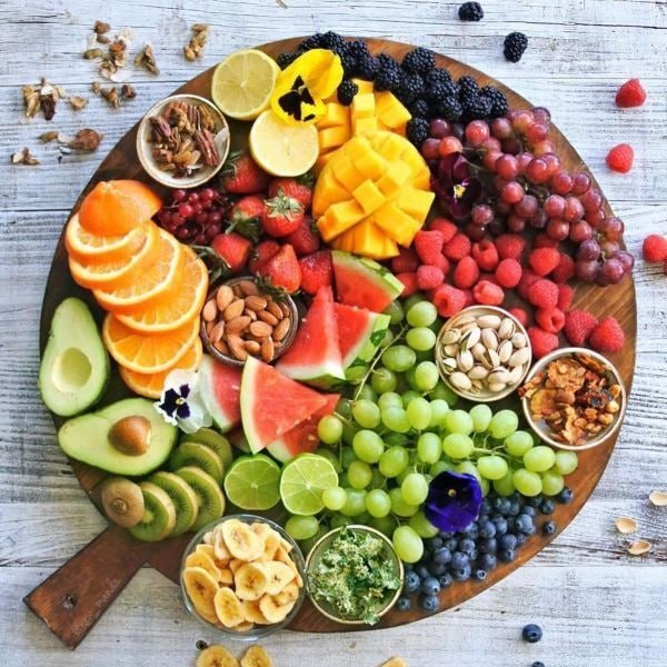 Colorful fruit and nut platter on wooden board with grapes, berries, citrus, tropical fruits, and assorted nuts