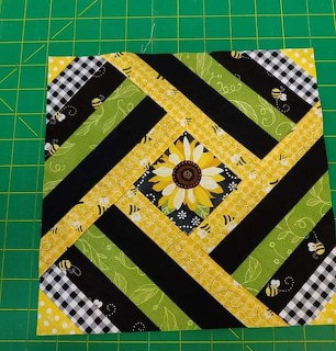 Quilted fabric block with diagonal strips in yellow, green, black with gingham and sunflower center on green cutting mat