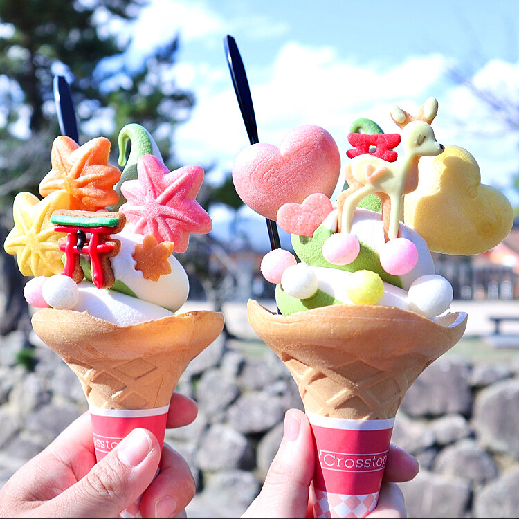Two hands holding colorful decorated dessert cones with pastel candy toppings outdoors