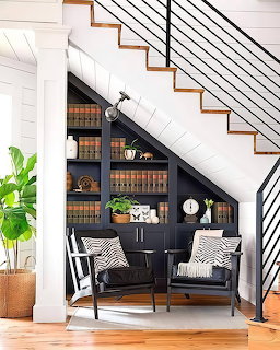 Cozy reading nook with dark built-in bookshelves under a staircase, two chairs with striped pillows