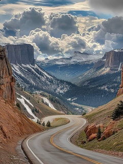 Winding paved road through steep mountain pass with dramatic cliffs, valleys, and clouds